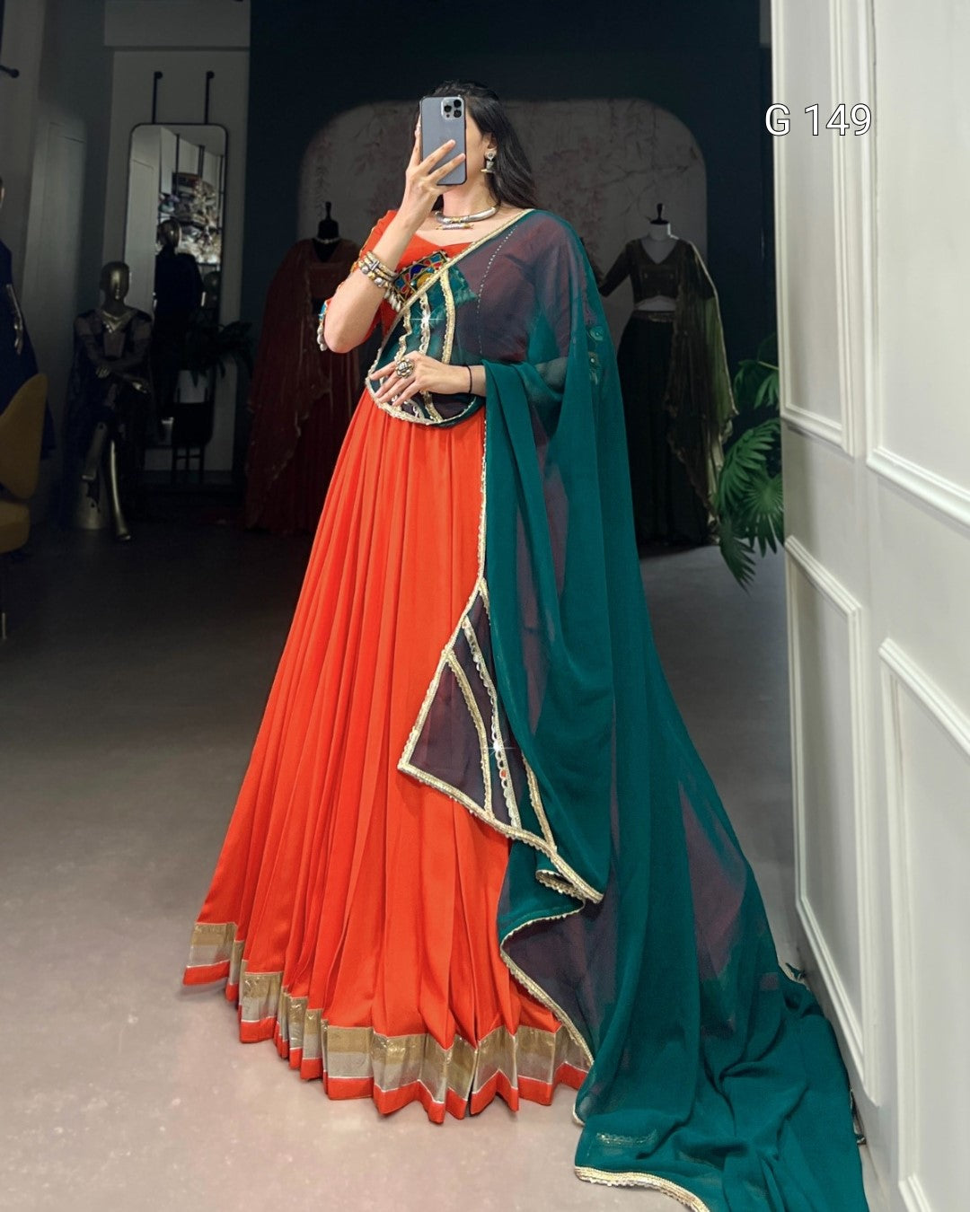 Person wearing a traditional outfit with an orange saree and green dupatta in a room.