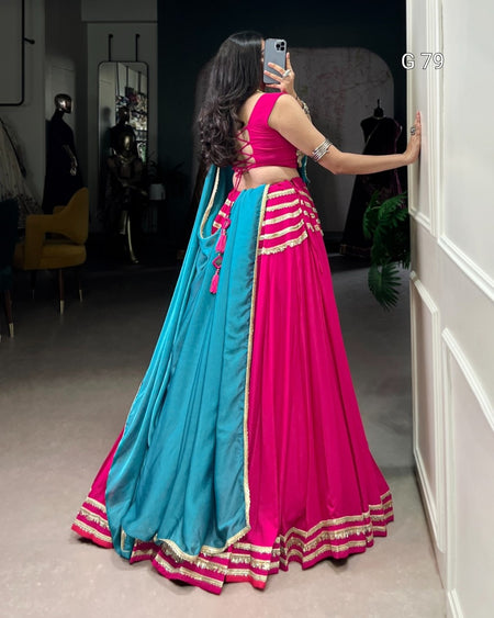 Woman wearing a pink and blue traditional outfit, standing in a room.