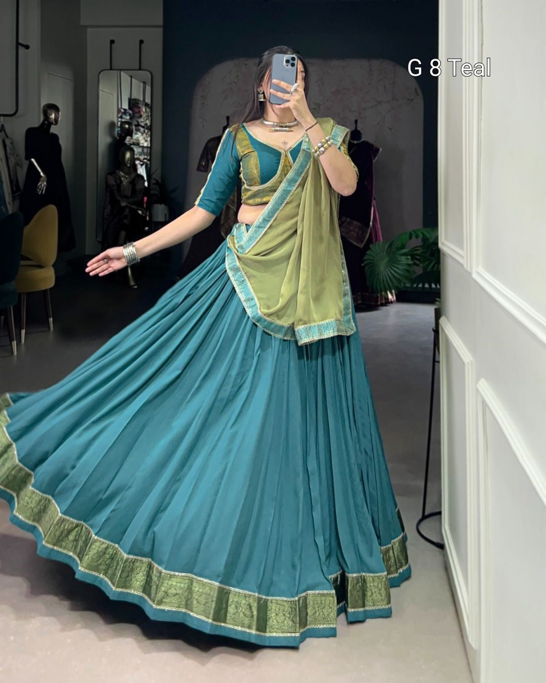 Woman wearing a blue and green traditional outfit in a room.