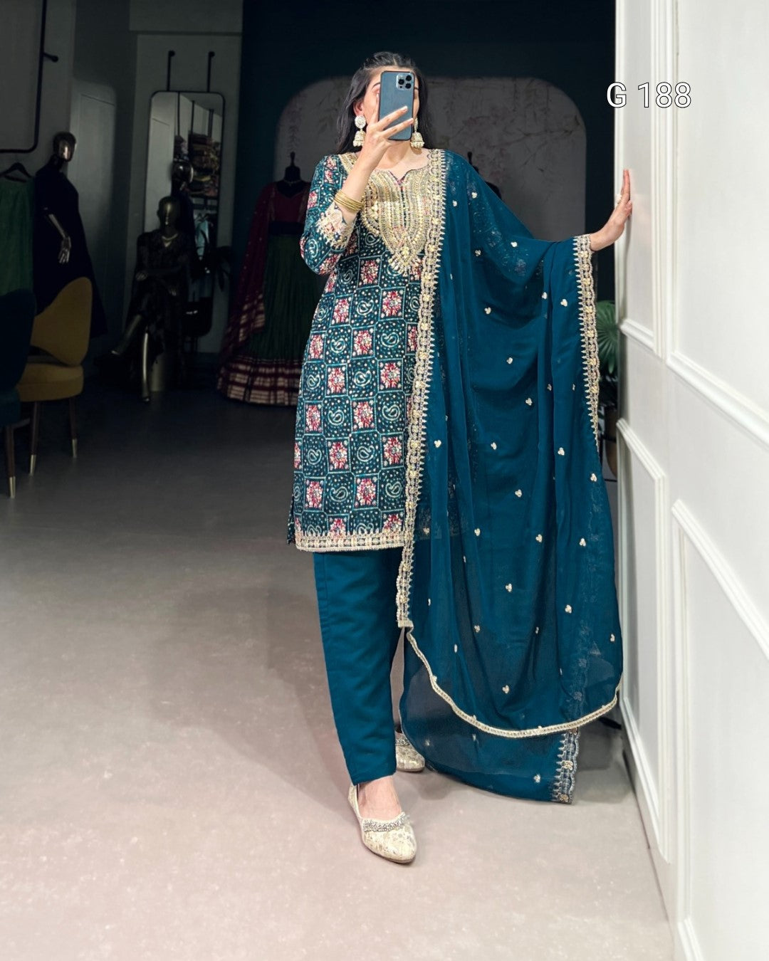 Person wearing a traditional blue and green outfit with intricate patterns in a room.