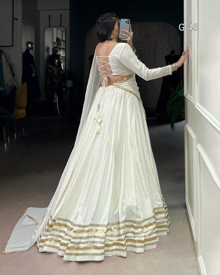 Person wearing a white and gold traditional outfit in a room.