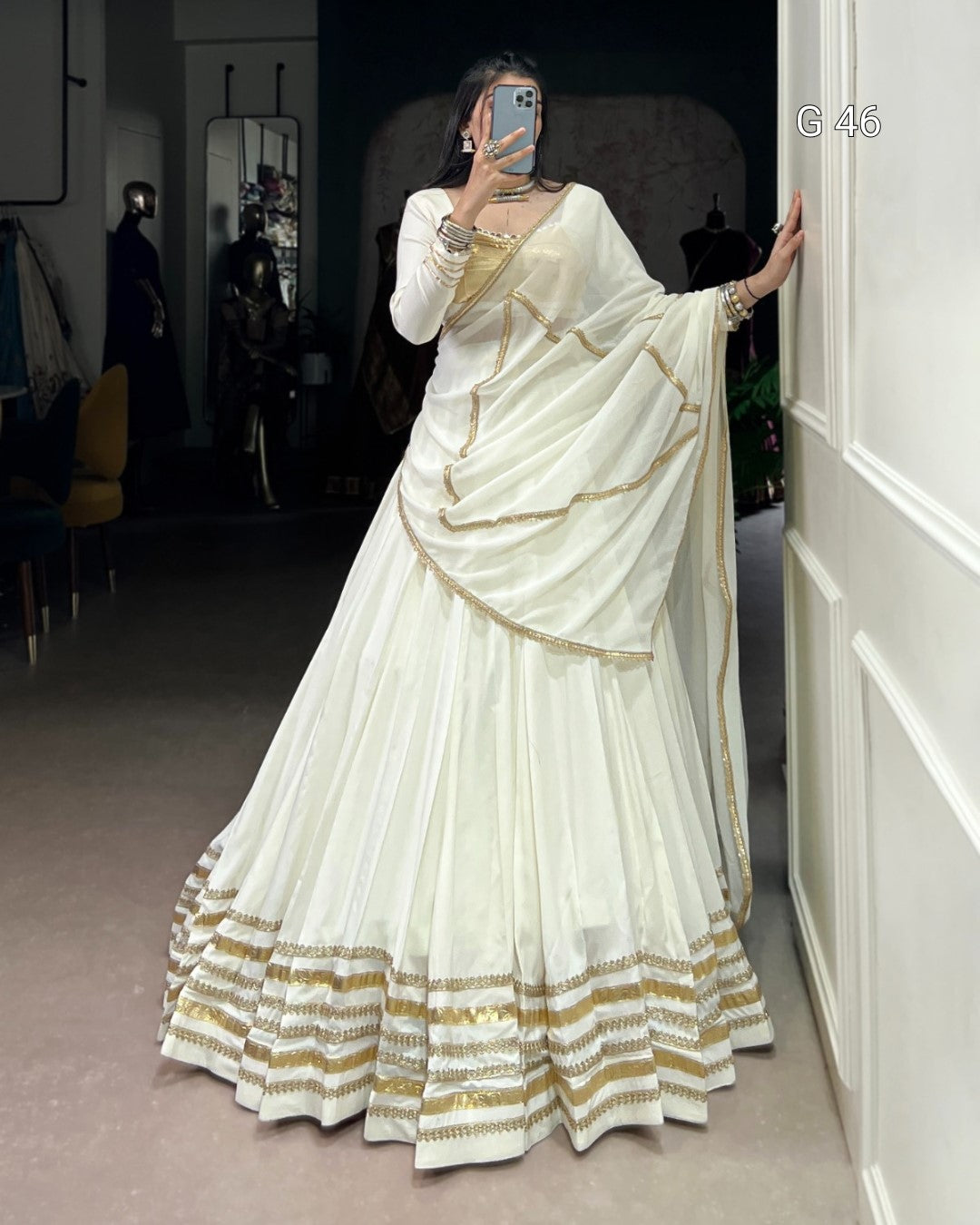 Woman wearing a white saree with gold accents in an indoor setting.