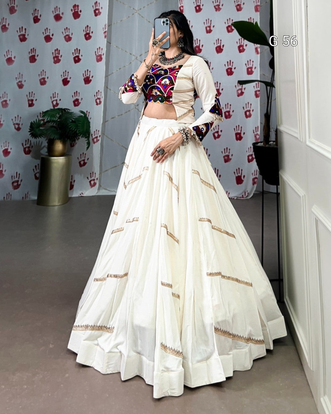 Person wearing a traditional outfit with a white skirt and colorful top in front of a patterned wall.