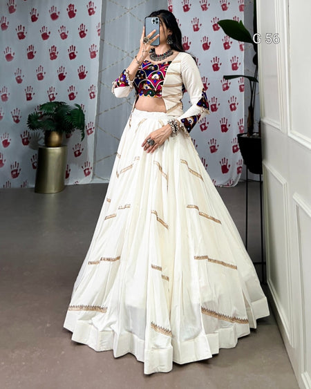 Person wearing a traditional outfit with a white skirt and colorful top in front of a patterned wall.