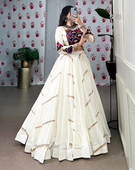 Person wearing a white traditional outfit with colorful top in a room with patterned wallpaper.