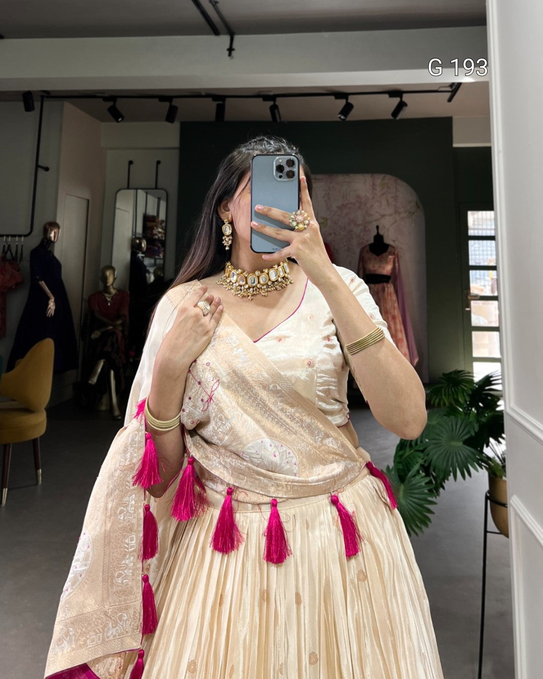 Woman in a traditional outfit with gold jewelry and pink tassels in a room.