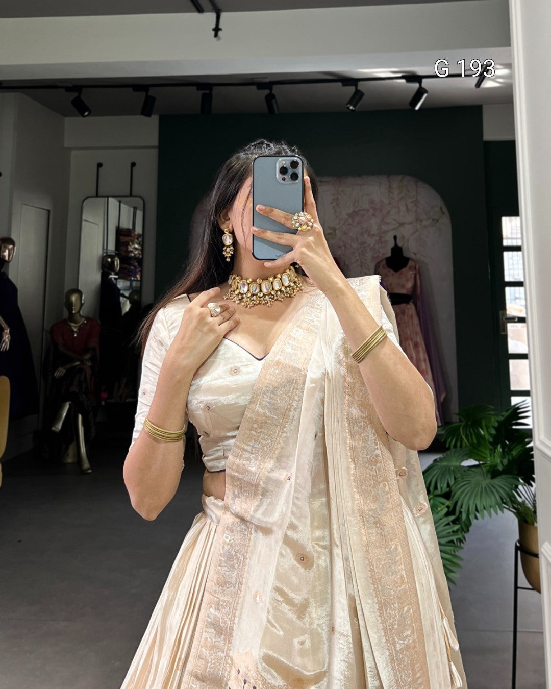 Woman in a beige saree with jewelry taking a mirror selfie in a store.