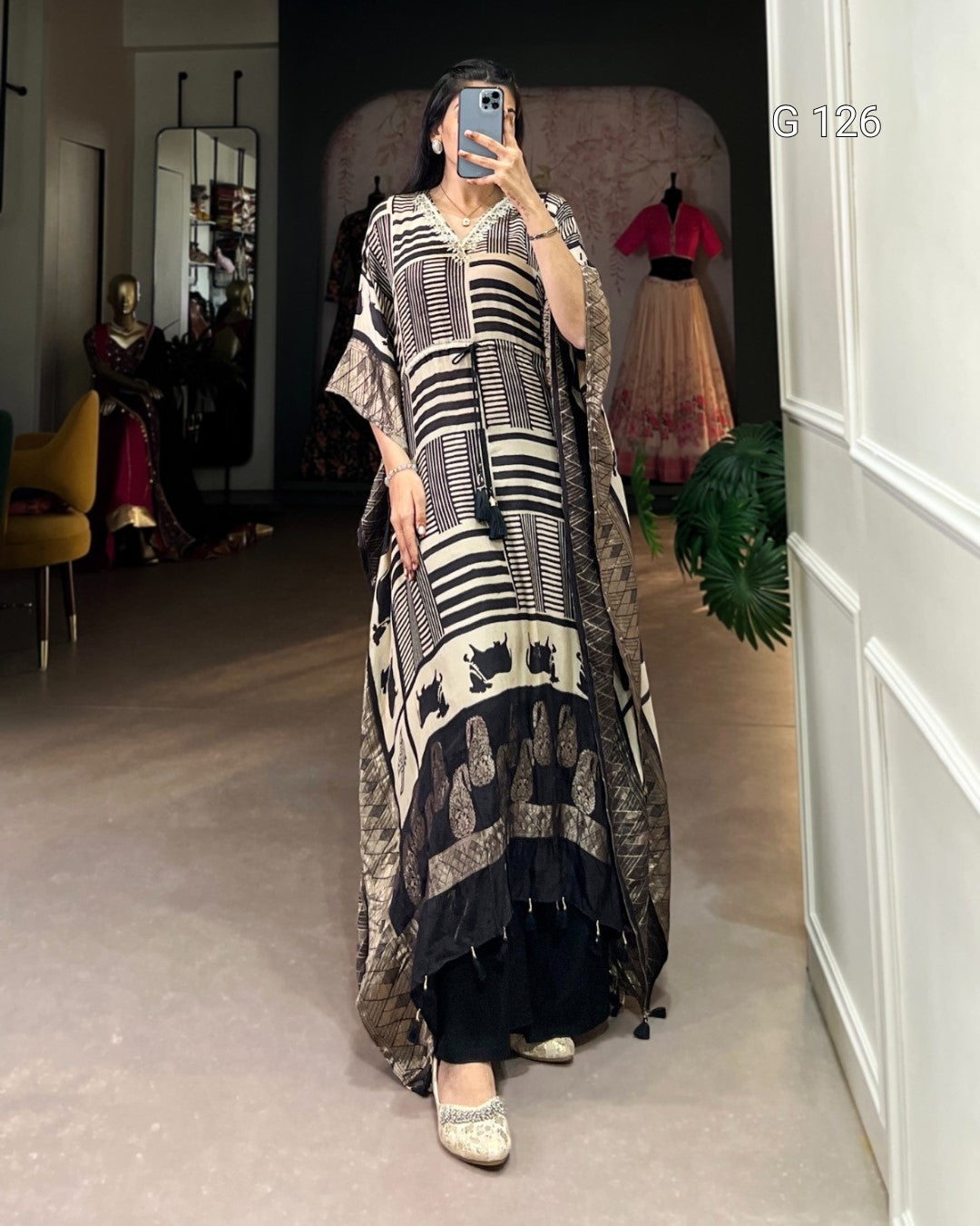 Person wearing a long, patterned dress in a room with a mirror and clothing in the background.