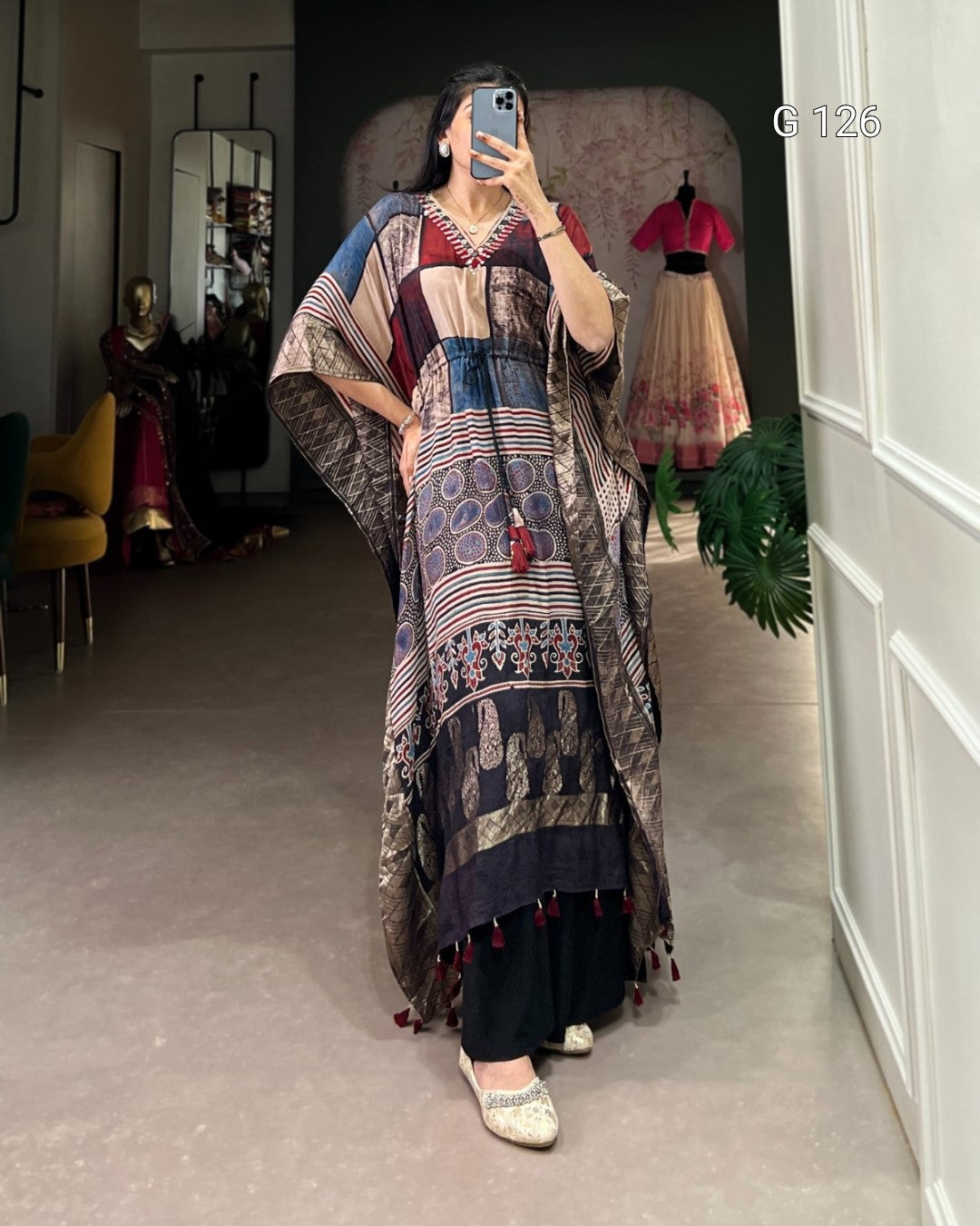 Person wearing a long, patterned dress standing in a room with a mirror and furniture.