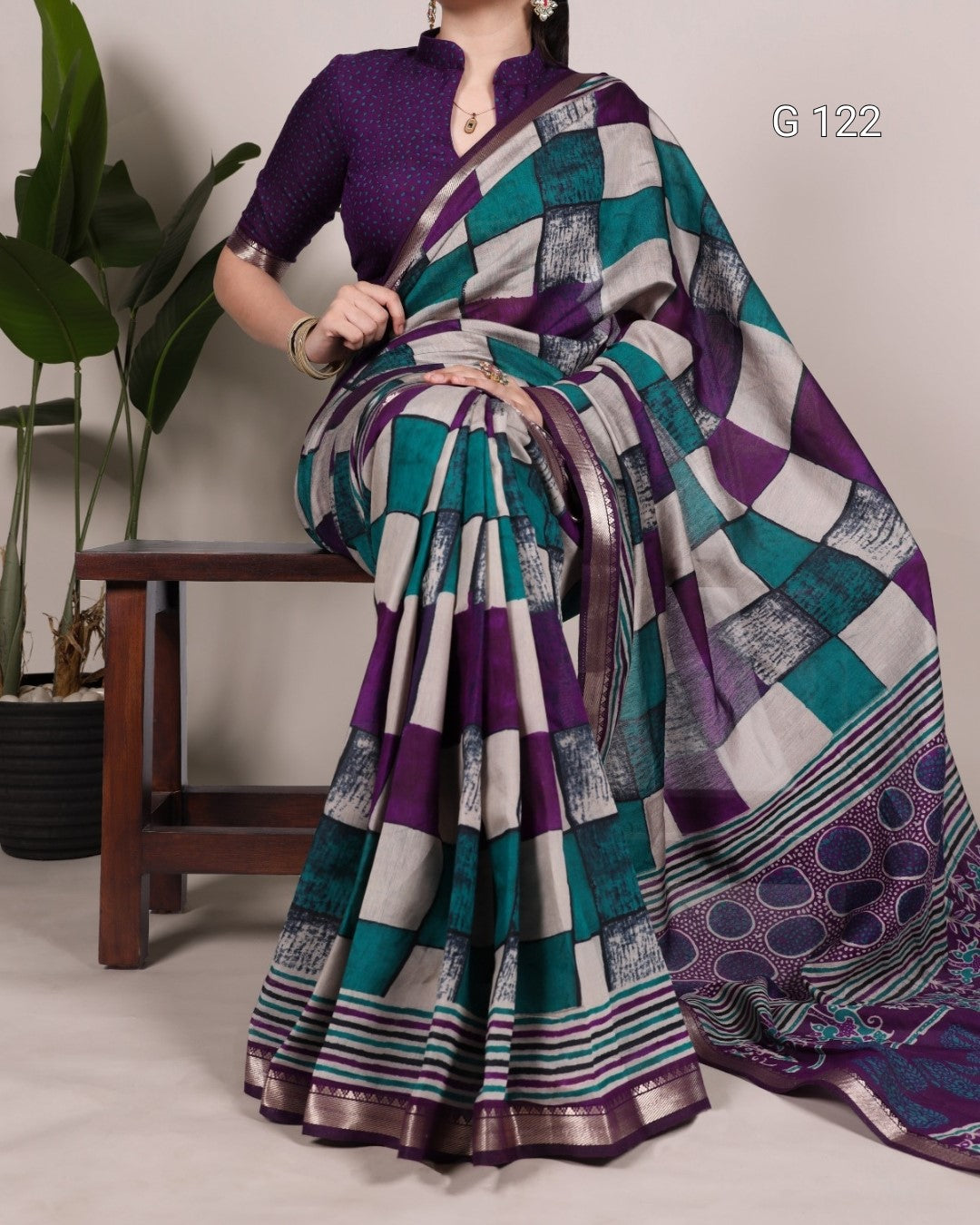 Woman wearing a colorful saree with a patterned design, sitting on a chair.