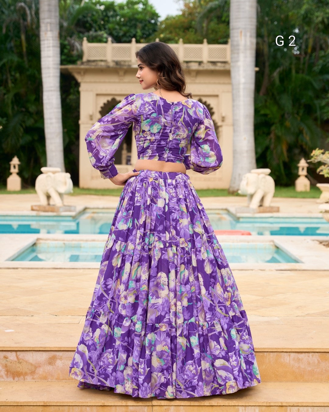 Woman in a purple floral dress standing by a pool with palm trees in the background