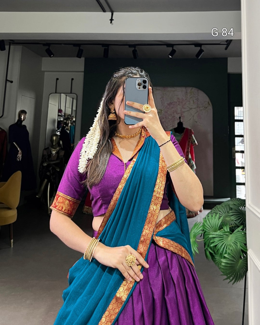 Person wearing a purple and blue saree with gold accents, taking a mirror selfie.
