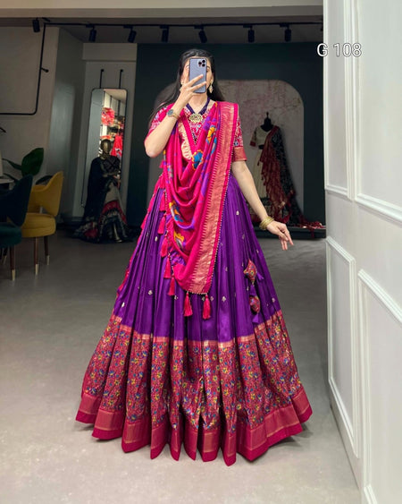 Person wearing a vibrant traditional outfit with a purple and pink color scheme in an indoor setting.