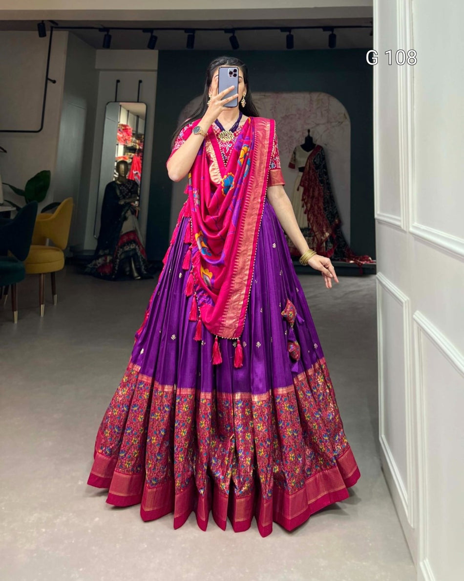 Person wearing a vibrant traditional outfit with a purple and pink color scheme in an indoor setting.