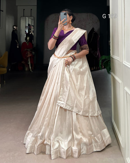 Woman wearing a white saree with a purple blouse in a room.