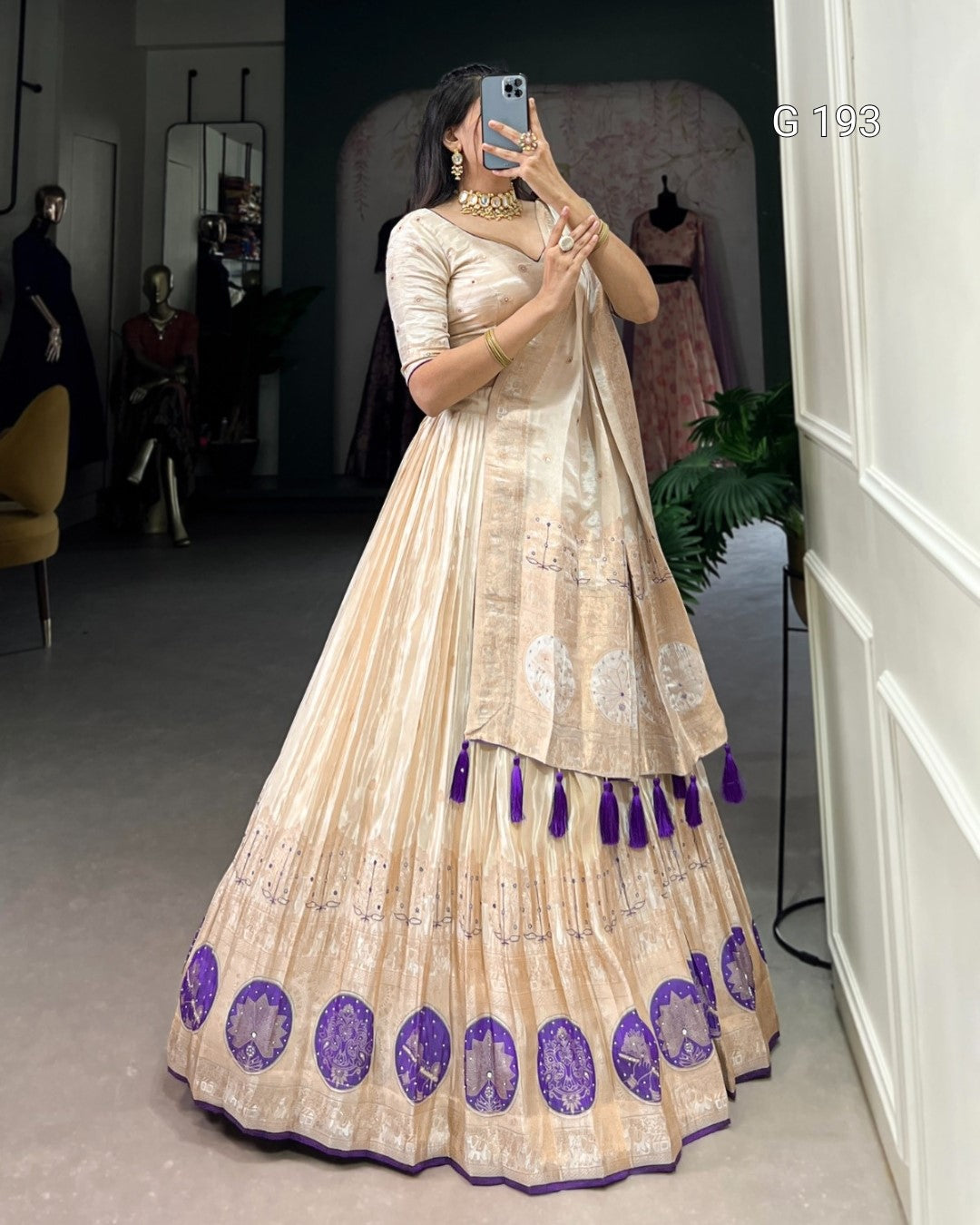 Woman wearing a beige and purple traditional outfit with tassels in a room.