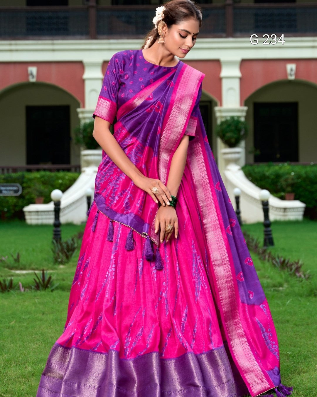 Woman wearing a pink and purple saree with a traditional building in the background