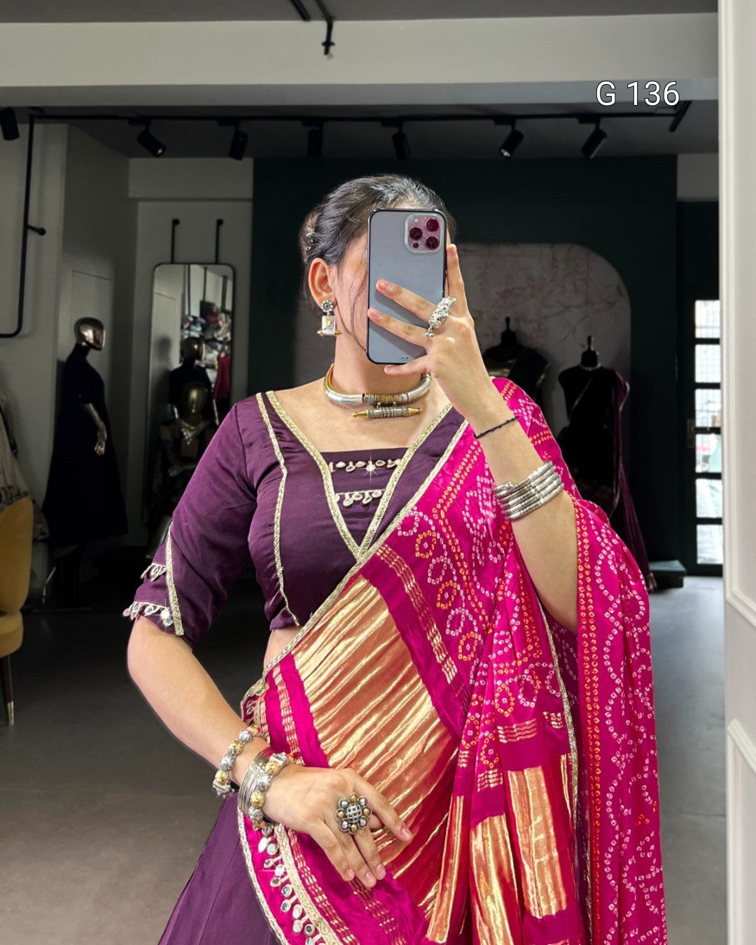 Woman taking a mirror selfie wearing a traditional saree in a store setting.