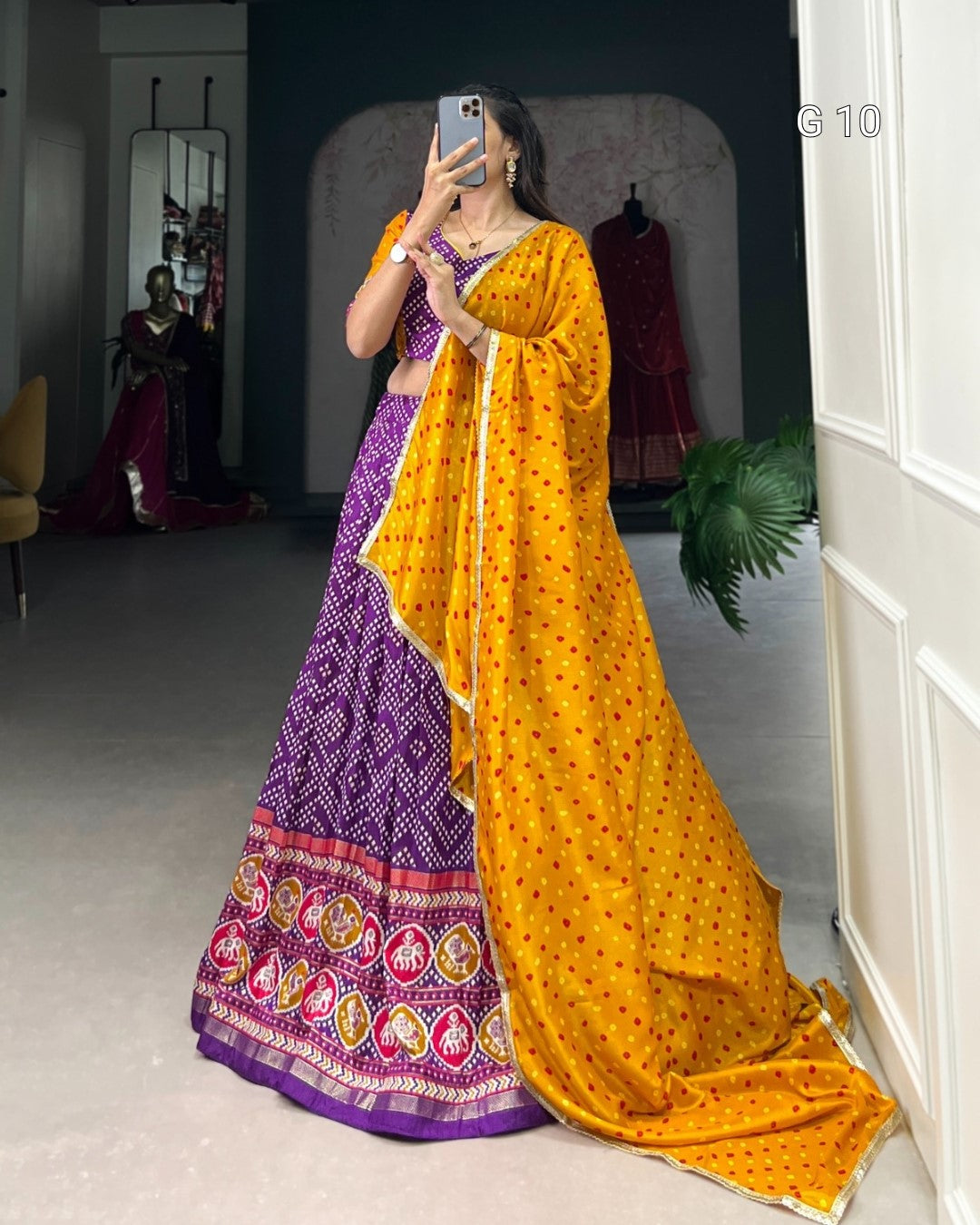 Woman in a yellow and purple traditional outfit taking a mirror selfie.