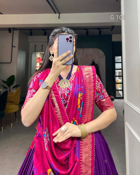 Person wearing a vibrant pink and purple traditional outfit with colorful patterns, standing indoors.