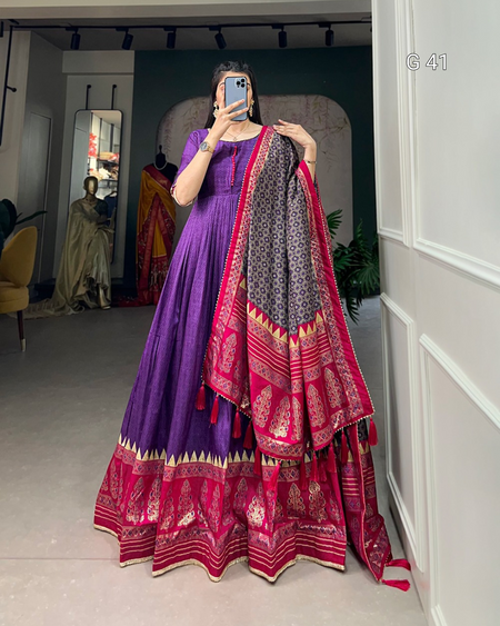 Person wearing a traditional outfit with a purple and pink saree in a room.