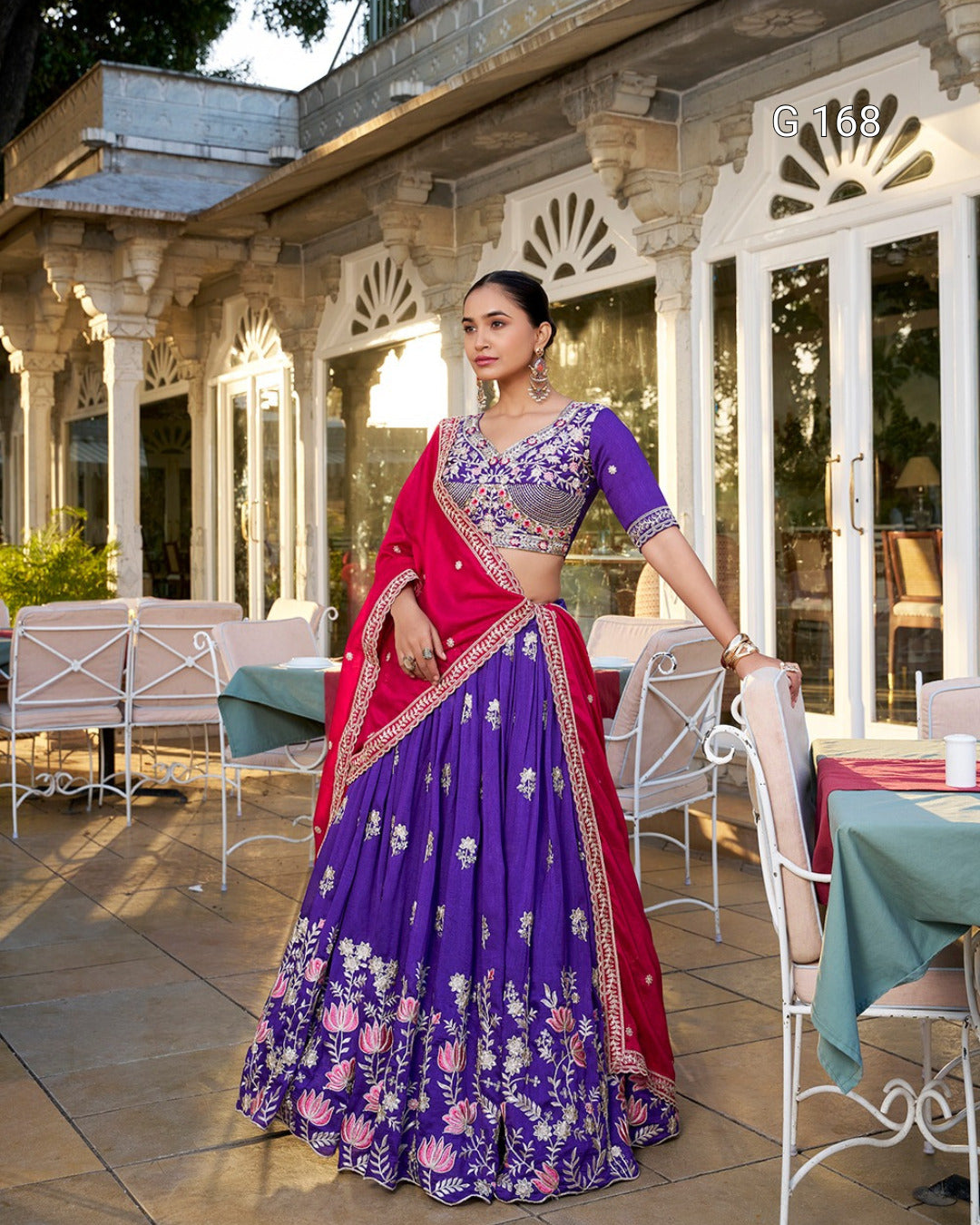 Woman in a traditional purple and red outfit standing outdoors in front of a building.