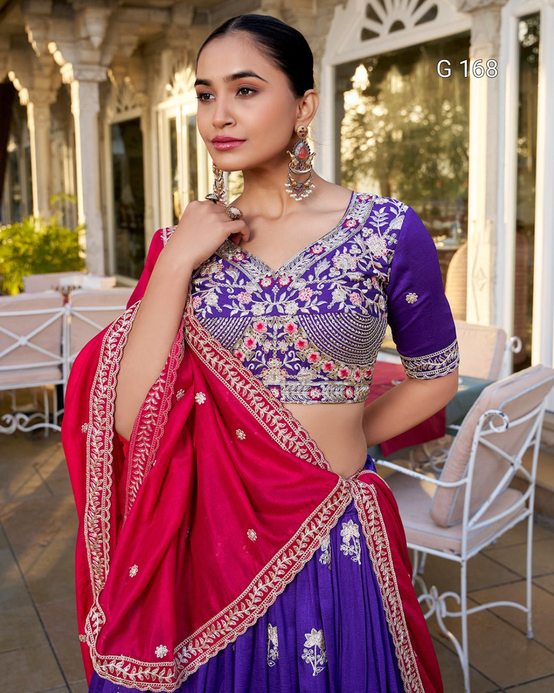 Woman wearing a traditional purple and pink saree with intricate designs, standing outdoors.