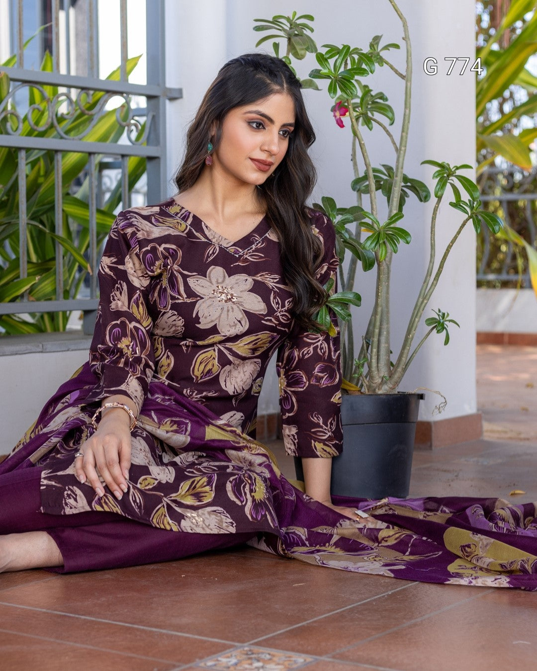 Woman in a purple floral outfit sitting on the floor with plants in the background