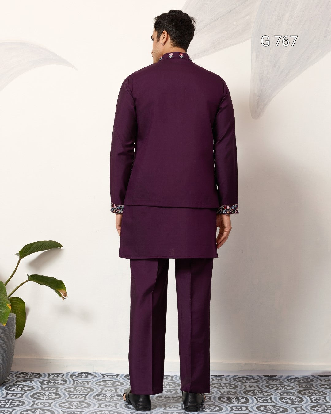 Man wearing a purple traditional outfit standing against a white wall.