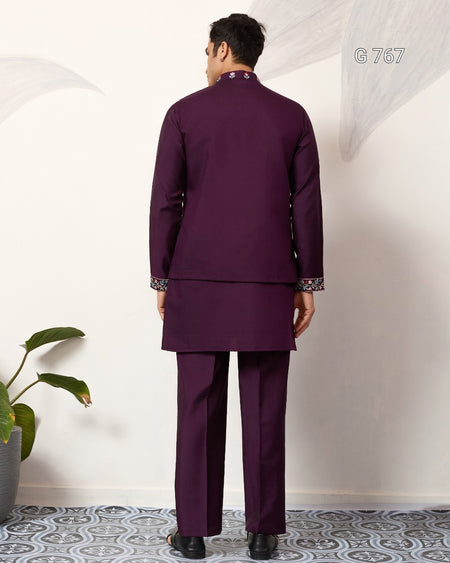 Man wearing a purple traditional outfit standing against a white wall.