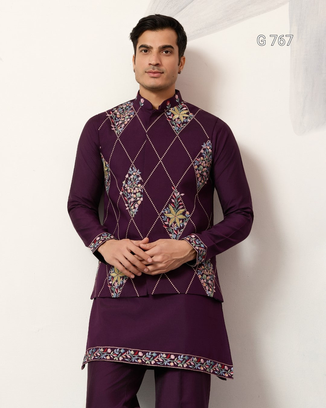 Man wearing a traditional purple outfit with intricate patterns on a white background