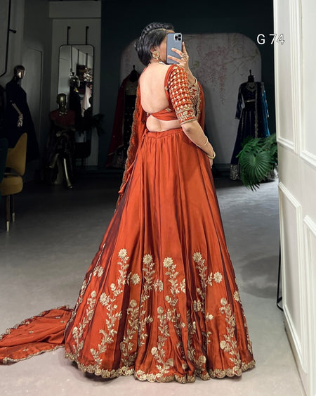 Person wearing a traditional orange outfit with gold embroidery in a room setting.