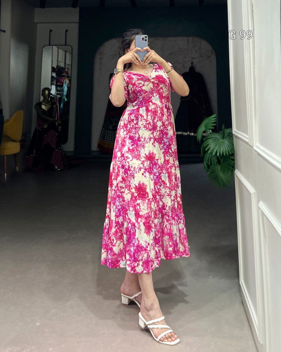 Person wearing a pink floral dress taking a mirror selfie in a room.