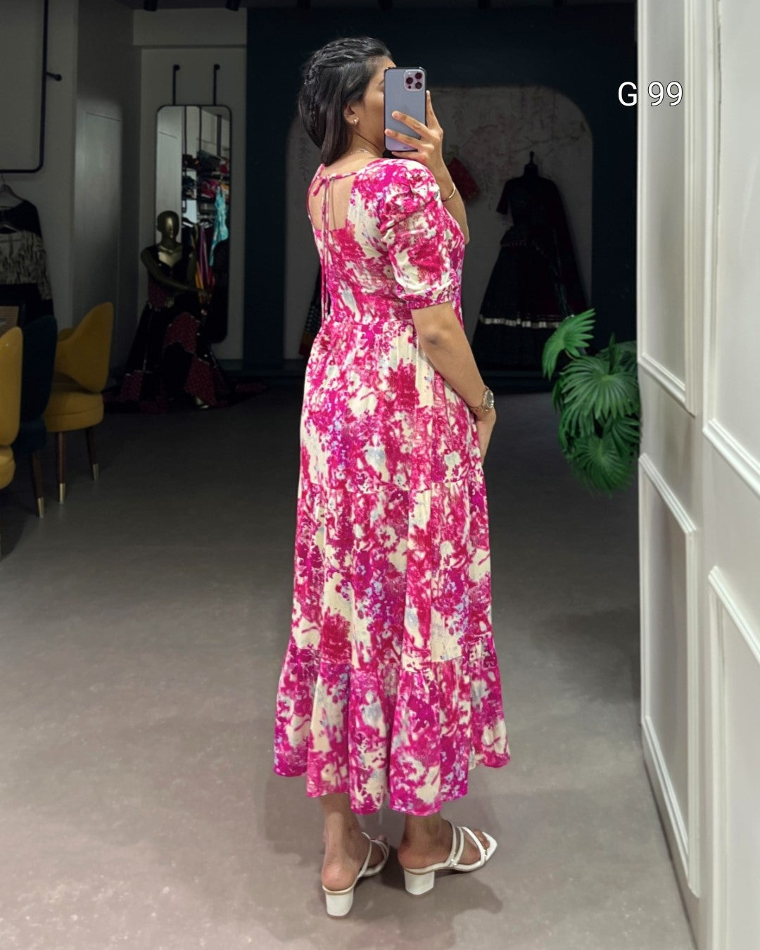 Woman taking a mirror selfie wearing a pink floral dress in an indoor setting.