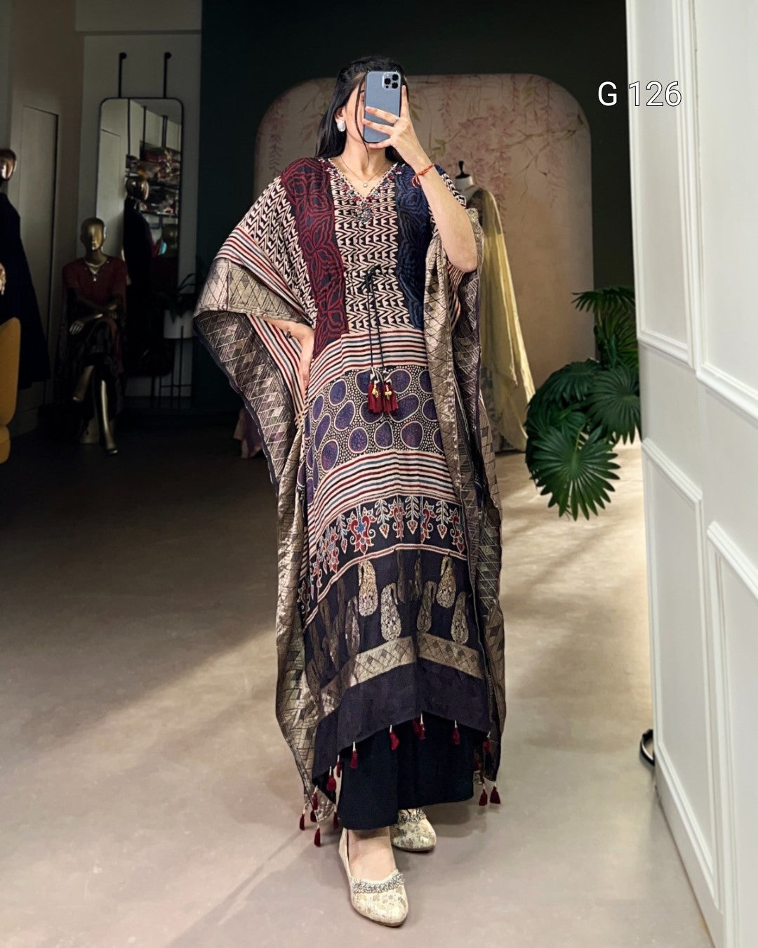 Person wearing a patterned dress taking a mirror selfie in a room.