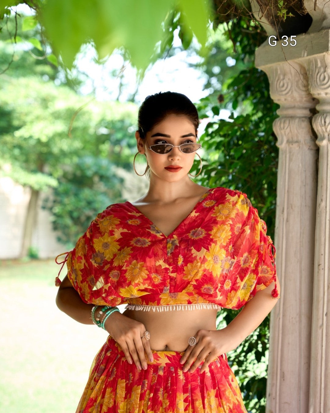 Woman wearing a red and yellow floral outfit with sunglasses, standing outdoors.