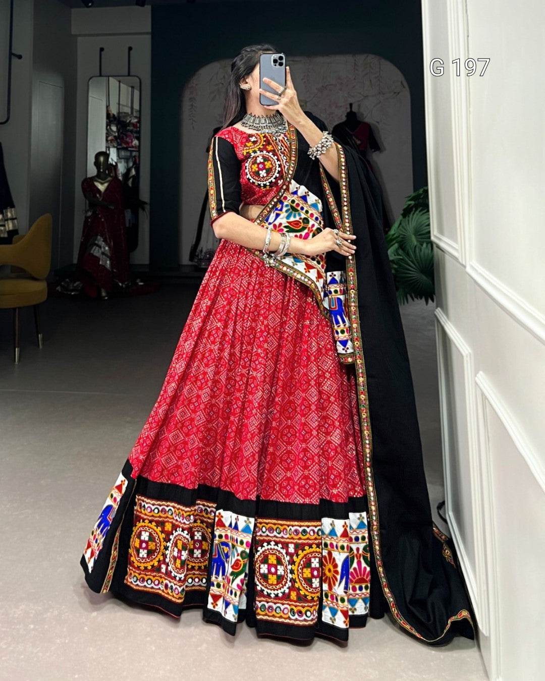 Person wearing a traditional red and black lehenga with colorful patterns in a room.