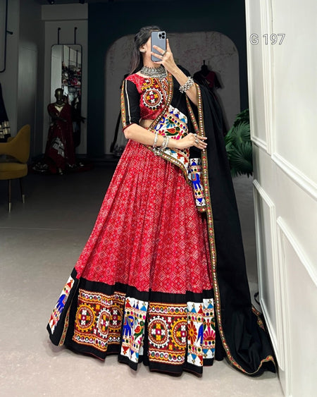 Person wearing a traditional red and black lehenga with colorful patterns in a room.