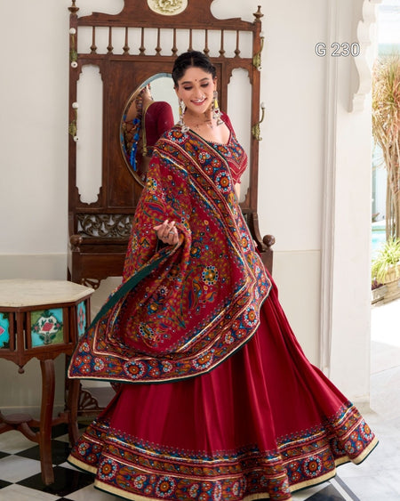 Woman in a red traditional outfit with colorful patterns standing in a room.