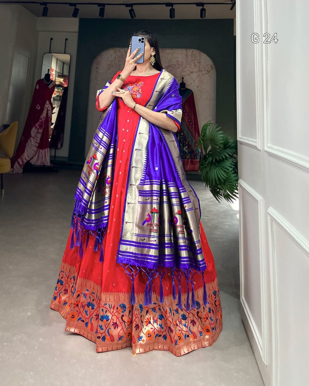 Woman wearing a traditional red and blue saree in a room with a mirror and plant.