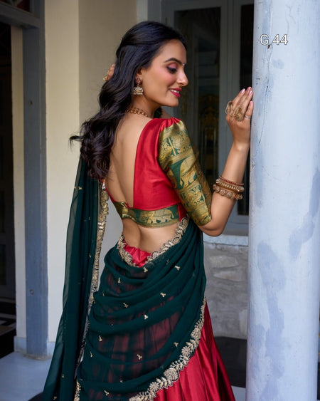 Woman in traditional red and green saree with gold blouse, standing indoors.