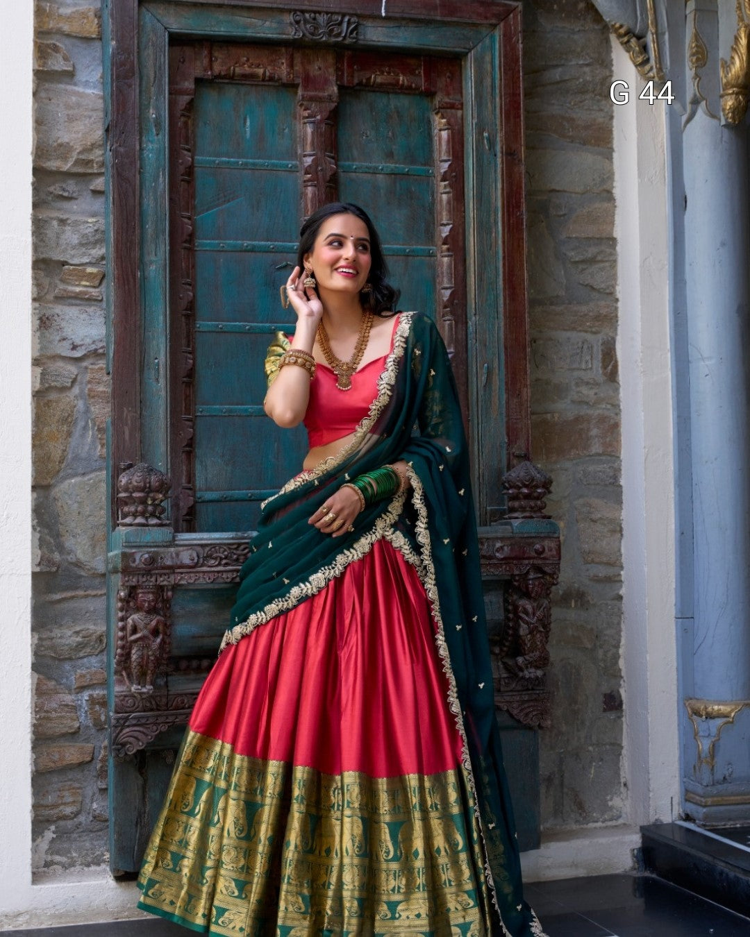 Woman in a red and green traditional outfit standing in front of a decorative door.