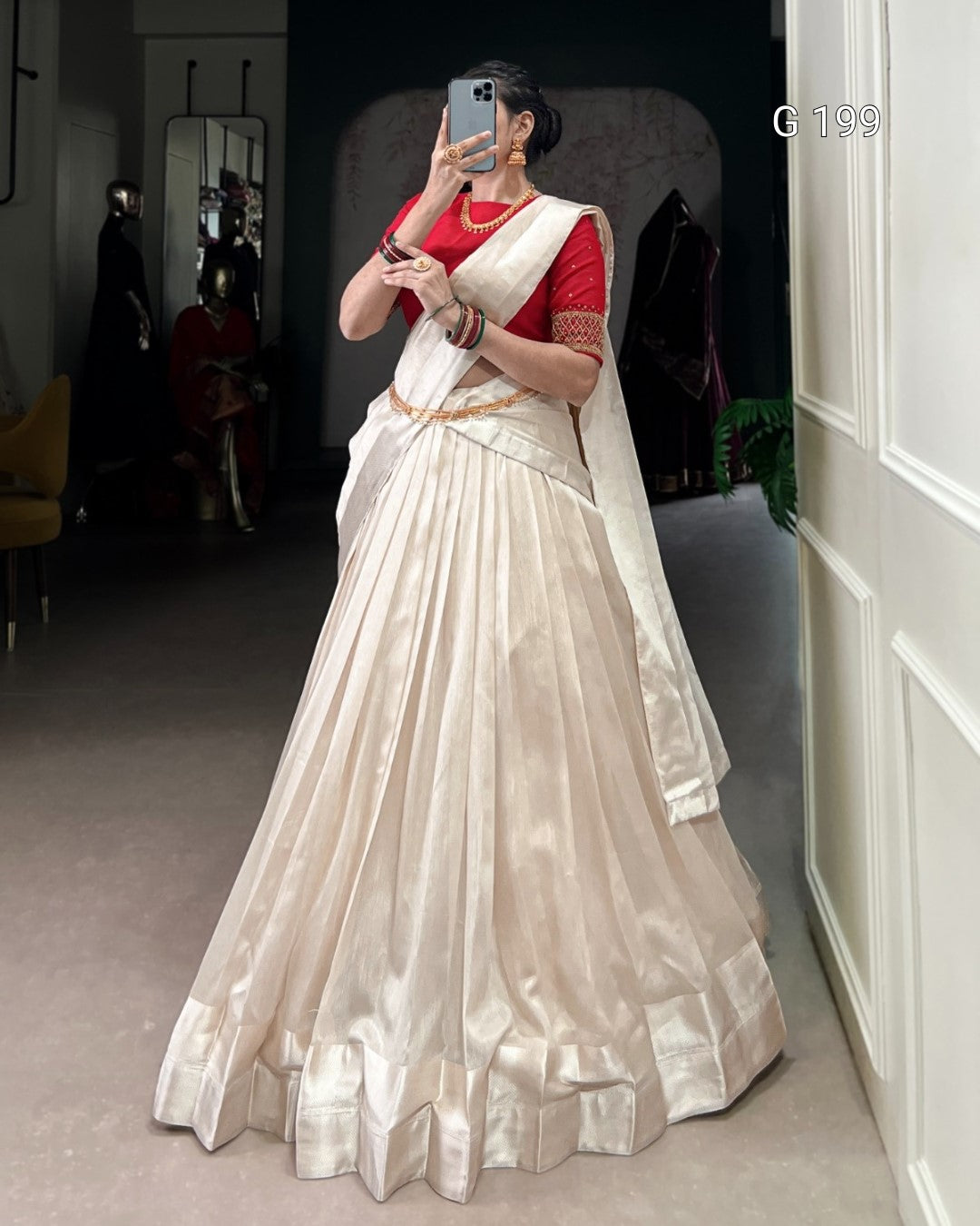 Person wearing a white saree with a red blouse in a room.