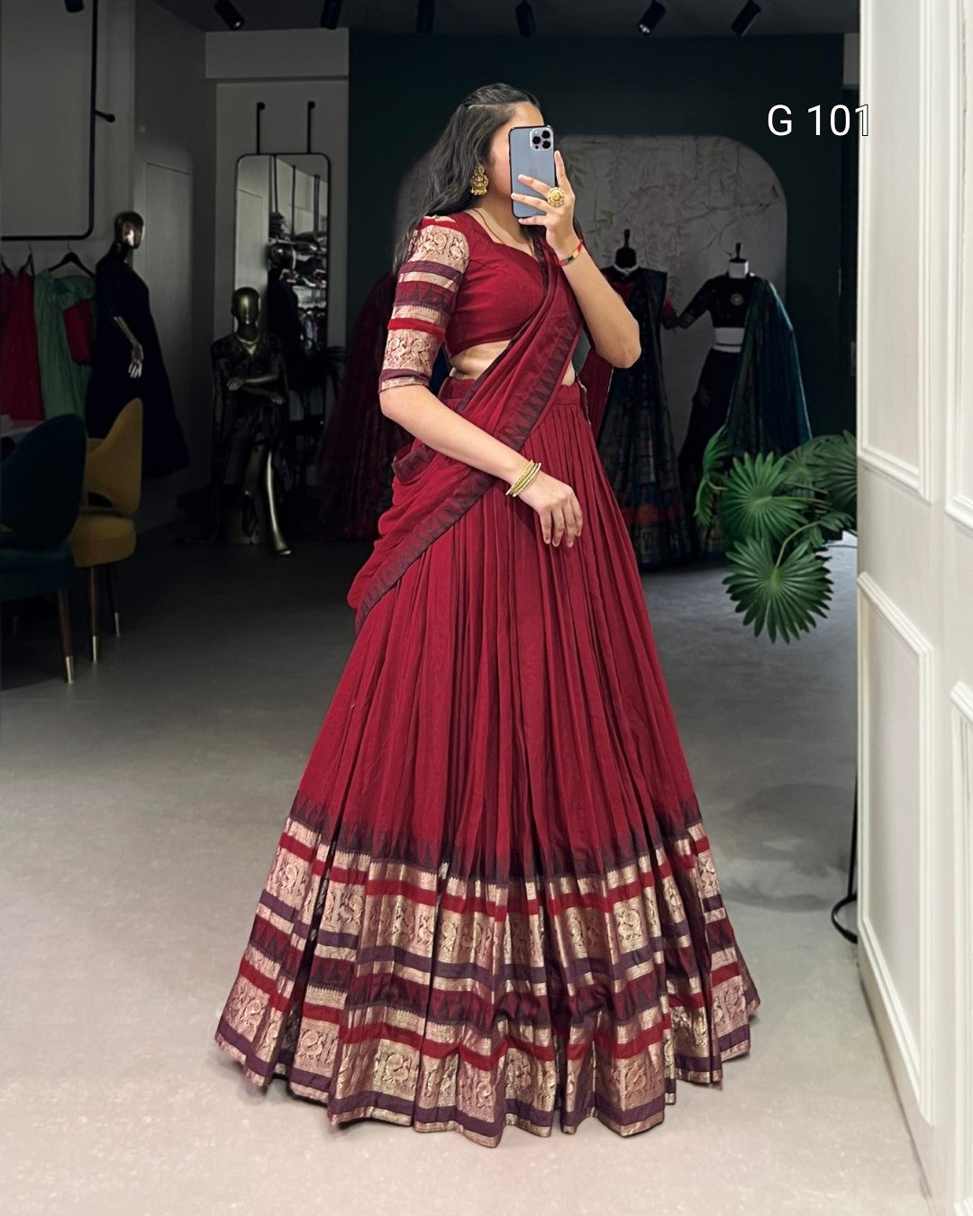 Woman wearing a red saree with gold patterns in a room with mirrors and clothing.