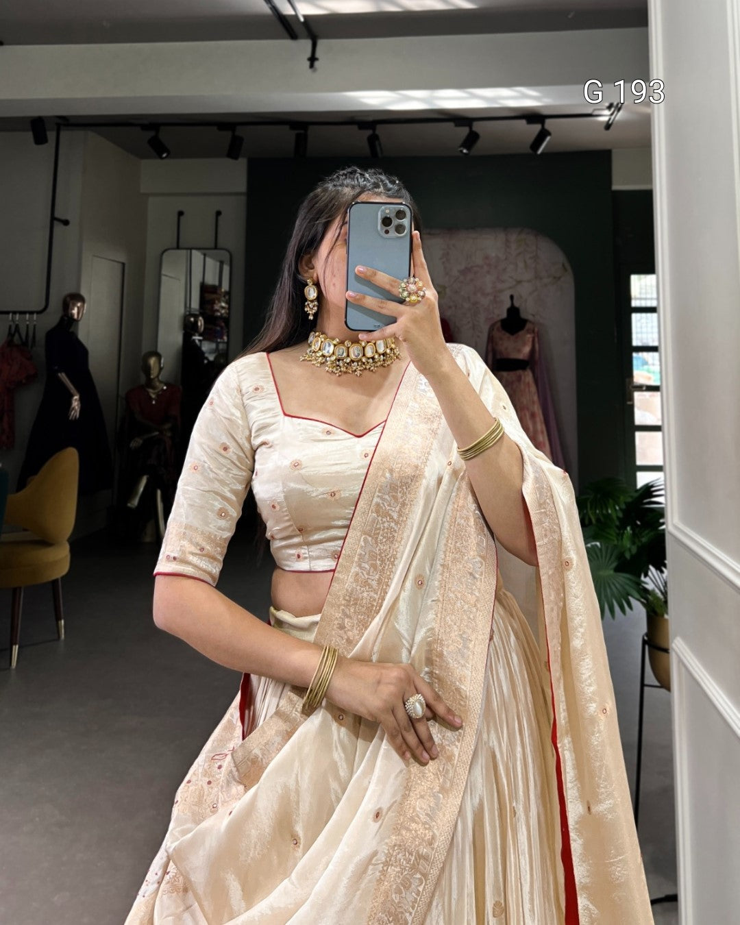 Person wearing a beige saree with gold jewelry in a store setting.