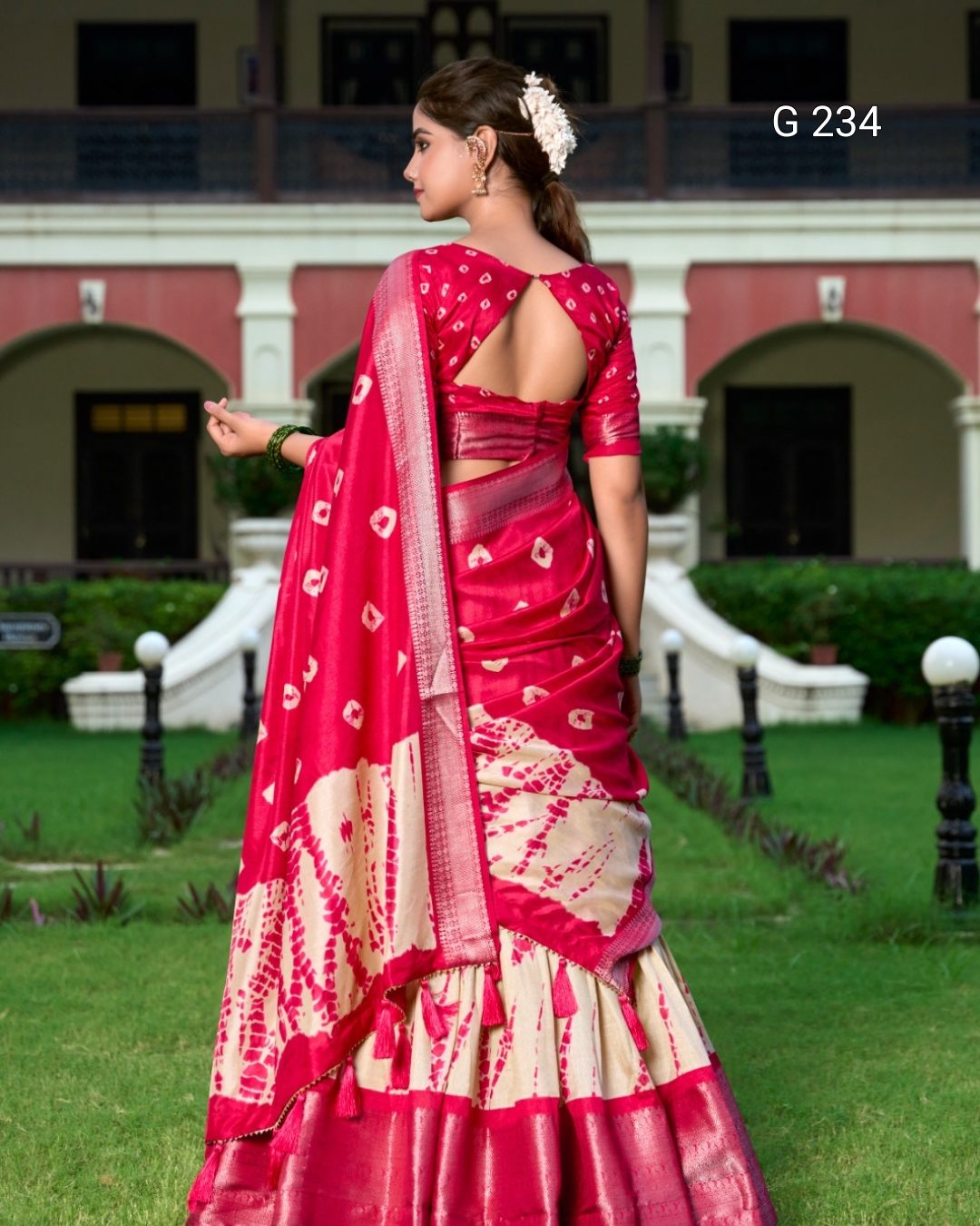Woman in a red and white saree standing outdoors with a building in the background