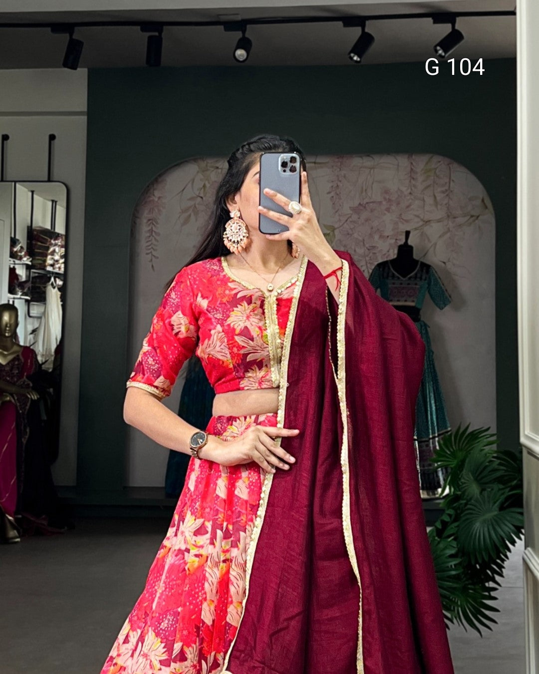 Woman in a red saree with floral patterns taking a mirror selfie in a store.