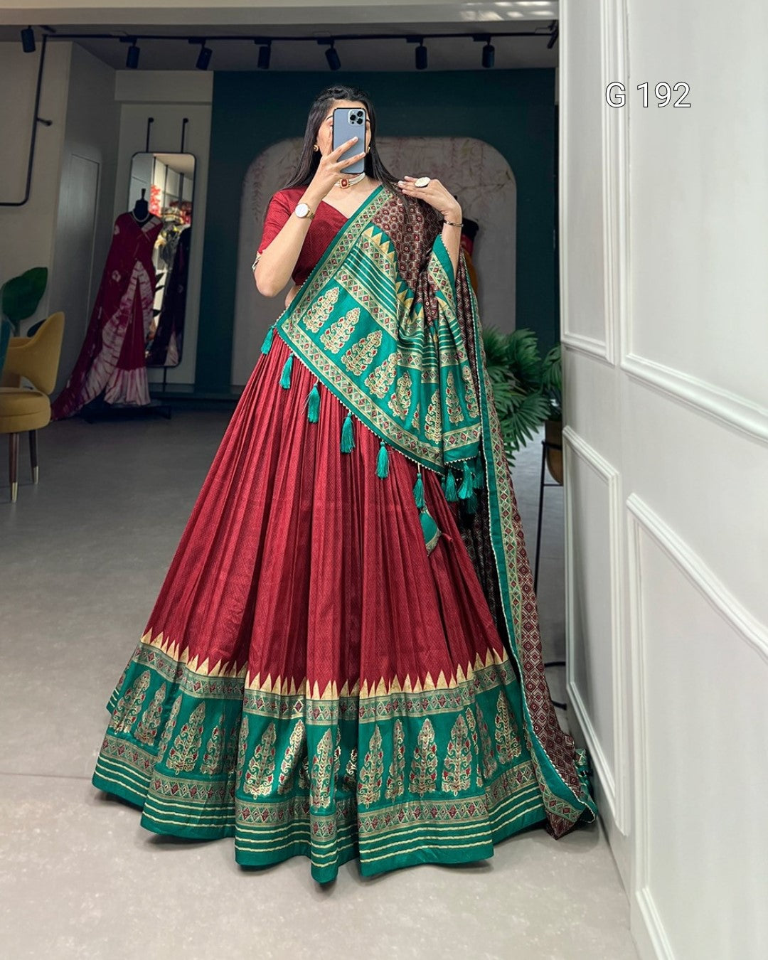 Woman wearing a red and green traditional outfit with a matching dupatta in a room.