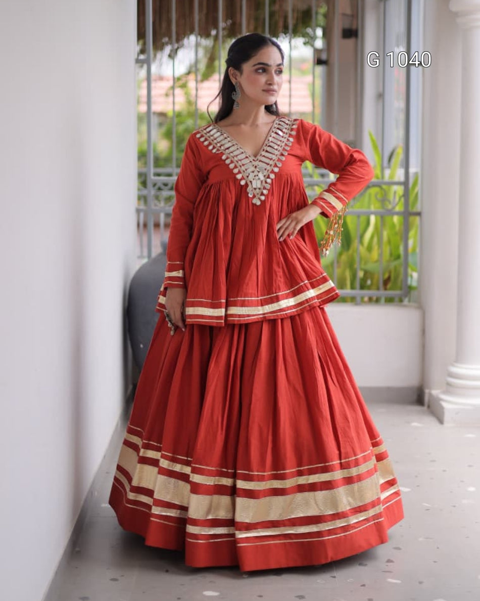 A woman models a traditional Indian outfit consisting of a red long kurta and a matching flared skirt with beige and white striped borders, set against a white-walled corridor with a window in the background.