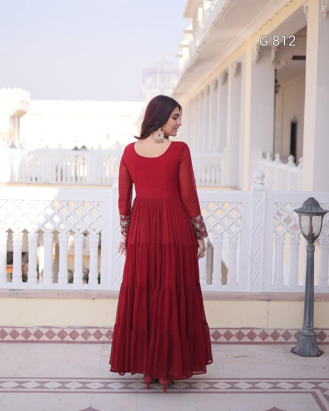 Woman in a red dress standing on a balcony with white railings and a lamp post.